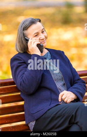 Positive senior Frau Reden auf dem Smartphone draußen im Park. Fokus auf smart phone! Stockfoto