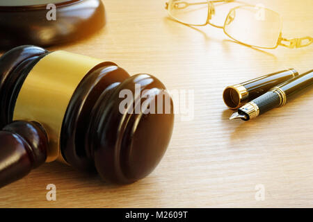 Gesetz Konzept. Richter Hammer, Pen und Gläser auf einem hölzernen Schreibtisch in einem Gerichtssaal. Stockfoto