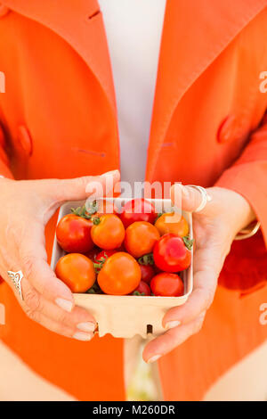 Frau Einkaufen für frisches Gemüse produzieren zu einem Bauernmarkt. In der Nähe der Hände halten ein Pint Warenkorb Container mit Reifen bio Kirschtomaten. Stockfoto