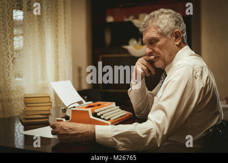 Nachdenklich retro älterer Mann am Schreibtisch neben veralteten Schreibmaschine und Denken zu sitzen. Stockfoto