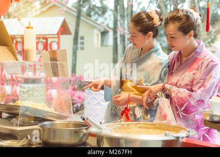 Attraktive Schönheit weibliche Reisende in traditioneller kimono Reisen in Japan zusammen und zeigen Snack stall Auswahl Dessert essen. Stockfoto