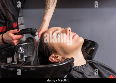 Weibliche stylist spült das Shampoo der jungen Frau, die in der Waschmaschine Waschbecken im Beauty Salon Stockfoto