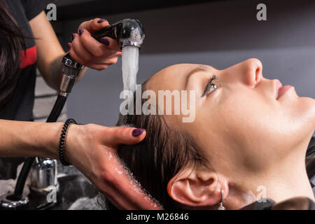 Close up Hände der weiblichen Stylist spült das Shampoo der jungen Frau, die in der Waschmaschine Waschbecken im Beauty Salon Stockfoto