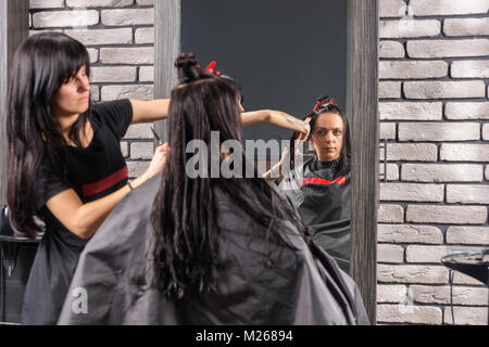 Weibliche Friseur schneiden und Modellierung braunes Haar von Schere und Kamm von Junge brünette Frau, während sie sitzt in einem Sessel im Beauty Salon Stockfoto