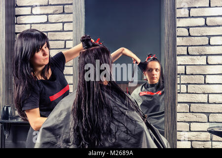 Attraktiven weiblichen Friseur schneiden und Modellierung braunes Haar von Schere und Kamm von Junge brünette Frau, während sie sitzt in einem Sessel in der Schönheit Stockfoto