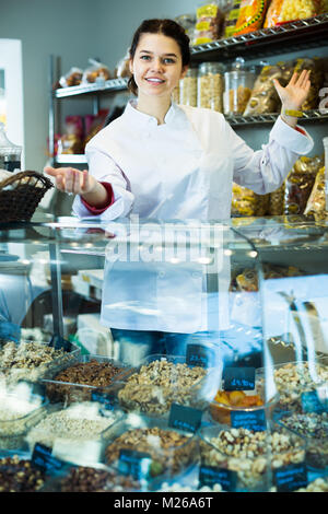Junge Verkäuferin zeigt eine große Auswahl an Muttern und süße Früchte, die in der STORE Stockfoto
