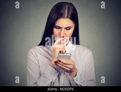 Junge Frau schaut verwirrt und ängstlich, während das Lesen von Nachrichten im Smartphone. Stockfoto
