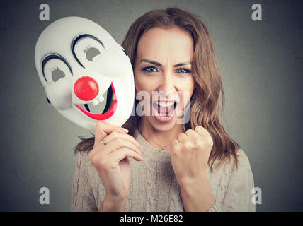 Junge Frau mit clown Maske und schreit Kamera auf Grau. Stockfoto