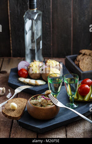 Wodka mit eingelegte Pilze auf dem Board. Auf hölzernen Hintergrund Stockfoto