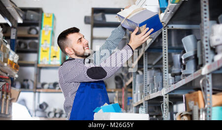 Junge fröhliche positiver Mann Arbeiter gehen durch Sanitärtechnik Details in der Werkstatt Stockfoto