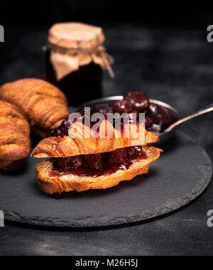 Croissant mit Erdbeer- füllung und Marmelade auf schwarzem Hintergrund Stockfoto