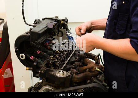 Ein junger Mann Lehrling arbeitet auf einem Auto Motor während der Ausbildung Mechaniker. Stockfoto