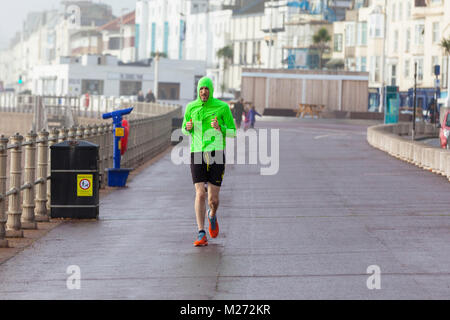 Ein Mann mit einem hell fluoreszierende Jacke entlang der Strandpromenade von Hastings im Winter auf einem feuchten und nassen Morgen. East Sussex, Großbritannien Stockfoto