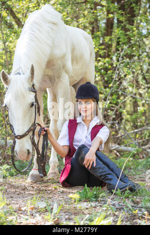 Schöne Frau auf dem Boden mit braunen Pferd neben ihr sitzen. Stockfoto