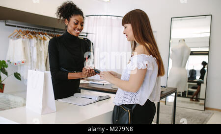 Kunden shopping Designer Verschleiß an eine Modeboutique. Kunden die Zahlung mit einer Kreditkarte auf einem Point of Sale. Stockfoto