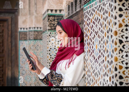 Lächelnd arabische Frau in traditioneller Kleidung mit roten Kopftuch auf ihrem Kopf arbeiten an Tablet Stockfoto