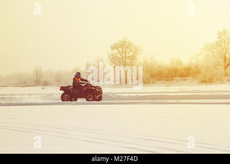 Die ATV-Reiter reitet auf dem Eis bei Sonnenuntergang im Winter, im Winter den zugefrorenen See. Winter reiten auf Motorräder. Kälte extreme. schöne Natur Winter Stockfoto