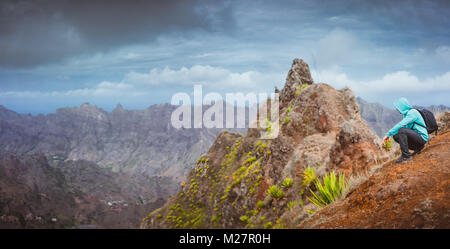 Mann Wanderer mit Rucksack sitzt auf dem Berg und im Tal. Atemberaubende karge Landschaft auf der Insel Santo Antao Cabo Verde Stockfoto