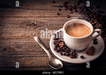 Eine Tasse Kaffee auf alten hölzernen Tisch mit ein paar Bohnen einen Löffel und eine Stange Zimt Stockfoto