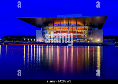 Blaue Stunde Kopenhagen Dänemark mit Hafenblick Oper leuchtet am Ocean widerspiegelt. Leichte Spuren von Boot in Rot im Vordergrund. Stockfoto