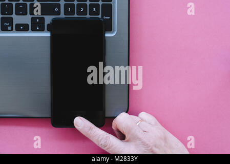 Mockup von Handy mit leeren Kopie Raum Bildschirm mit Laptop und Frau hand auf rosa Hintergrund. Flach, Ansicht von oben Stockfoto