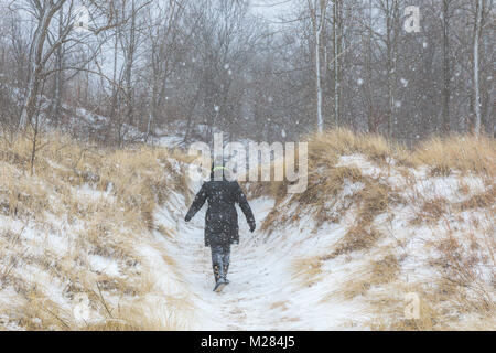 Woman in Black Winter Jacke und Hut wandern durch verschneite Sanddünen entlang des Lake Michigan in einem Winter Schnee Sturm Stockfoto