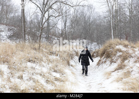 Woman in Black Winter Jacke und Hut wandern durch verschneite Sanddünen entlang des Lake Michigan in einem Winter Schnee Sturm Stockfoto