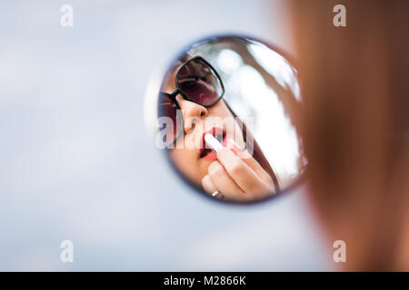 Frau Anwendung Lippen Make-up mit Hilfe Ihrer scooter Spiegel. Defokussiertem Hintergrund. Stockfoto