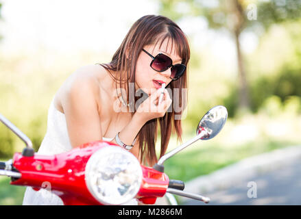 Frau Anwendung Lippen Make-up mit Hilfe Ihrer scooter Spiegel. Defokussiertem Hintergrund. Stockfoto