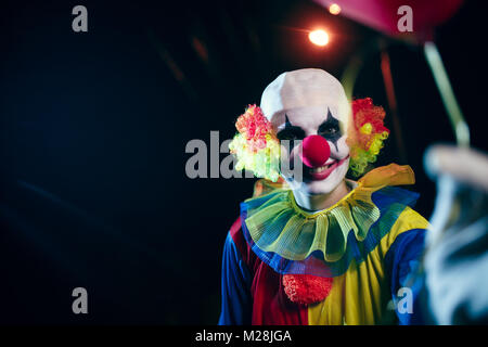 Foto von Clown mit roten Ballon in der Nacht auf der Straße Stockfoto