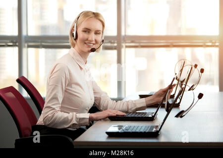 Weibliche Fahrer mit Headset lächelnd. Erwachsene Frau Sekretär mit Kopfhörern tun Kundendienst in einem Callcenter. Stockfoto