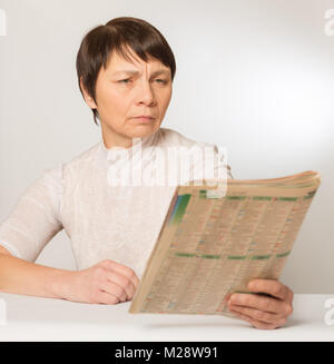 Presbyopie, Sehstörungen. Eine ältere Frau ohne Brille liest eine Zeitung ihre Wegdrücken Stockfoto