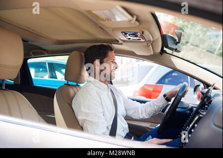 Lächelnden jungen Mann saß in seinem Auto fahren durch die Stadt während seines morgendlichen Fahrt Stockfoto