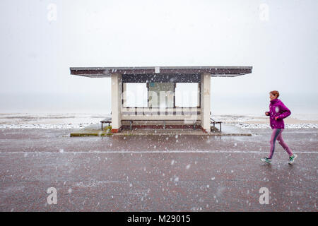 Llandudno, Wales, 6. Februar 2018. UK Wetter. Als eine gelbe Warnmeldung für Schnee für North Wales heute mit einigen Teilen von bis zu 8 cm auf höheren Boden vorhergesagt. Sehr ungewöhnlichen Schnee für die Seebad Llandudno in Nordwales entdeckt, als diese Frau an einer Promenade Tierheim im Resort © DGDImages/Alamy leben Nachrichten Stockfoto