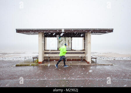 Llandudno, Wales, 6. Februar 2018. UK Wetter. Als eine gelbe Warnmeldung für Schnee für North Wales heute mit einigen Teilen von bis zu 8 cm auf höheren Boden vorhergesagt. Sehr ungewöhnlichen Schnee für die Seebad Llandudno im Norden von Wales als diese Person entdeckt worden jogging Vergangenheit eine Promenade Tierheim im Resort in schweren Schnee © DGDImages/Alamy leben Nachrichten Stockfoto