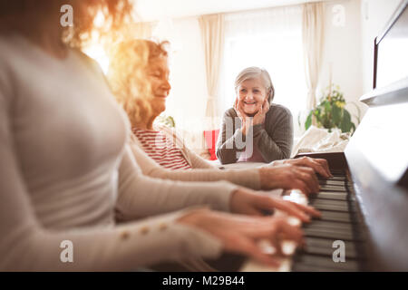 Ein Mädchen mit Mutter und Großmutter Klavier spielen. Stockfoto