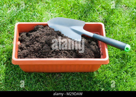 Brauner Topf mit Erde und Schaufel auf dem Gras Stockfoto