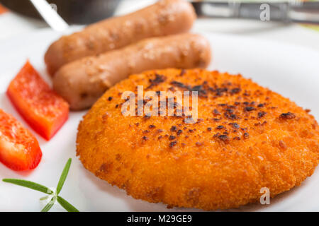 Hähnchen Cordon Bleu auf Platte mit zwei Würstchen und Rosmarin mit rotem Pfeffer Stockfoto