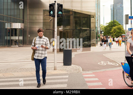 Junger Mann, Trinken einen Kaffee und senden eine SMS auf ein Handy, während eine Kreuzung in der Stadt Stockfoto
