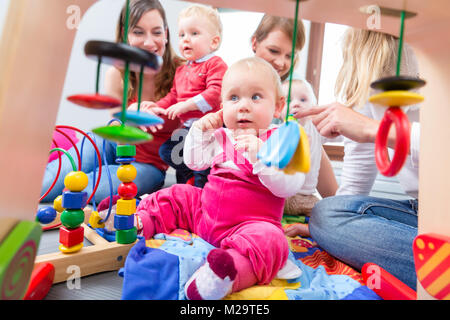 Porträt einer niedlichen Baby Mädchen suchen mit ihren schönen blauen Augen, während sie auf dem Boden sitzend mit zwei anderen Babys und ihre Mütter zu Hause Stockfoto