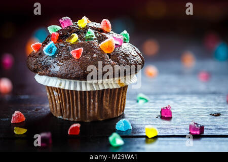 Lecker und lustig Chocolate Muffin mit Bonbons auf hölzernen Tisch. Bokeh Hintergrund selektiven Fokus. Stockfoto