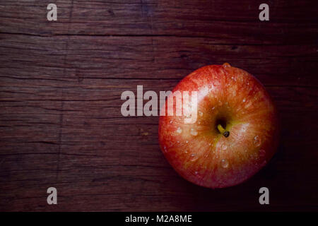 Roter Apfel mit Wassertropfen auf einem hölzernen Hintergrund Stockfoto