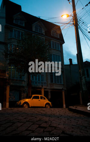 Ein gelber VW-Käfer beleuchtet durch eine Straßenlaterne in der Dämmerung in La Paz, Bolivien Stockfoto