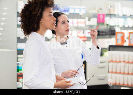 Seitliche Sicht auf zwei engagierte weibliche Apotheker suchen die beste Medizin im Lager beim zusammen in einer modernen Apotheke arbeiten Stockfoto