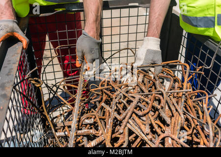 Zwei Arbeiter tragen gelbe harte Hüte und Sicherheit Warnwesten während der Prüfung ein Haufen rostigen Stahl Bars während der Arbeit auf der Baustelle Stockfoto