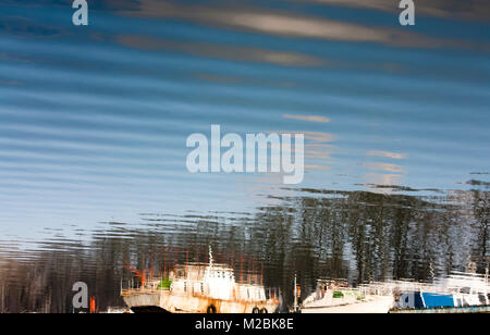 Unscharfe Reflexion verankert alte Boote, Bäume, blauer Himmel und Wolken im Wasser des Flusses Stockfoto