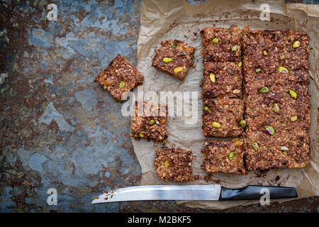 Hausgemachte Saatgut, Mutter, getrocknete Früchte und dunkle Schokolade Oat Energieriegel auf Backpapier auf schiefer Hintergrund Stockfoto