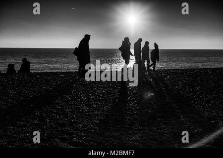 Silhouetten, die auf Brighton Beach im Winter mit der Sonne hinter Stockfoto