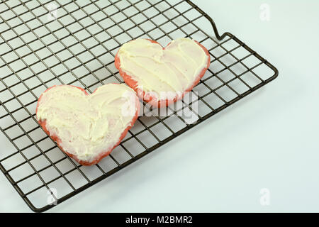 Zwei gebackene rote Herzen valentine Zucker vanille Cookies mit weißer Zuckerglasur auf Kühlung Rack auf weissem Holztisch Stockfoto