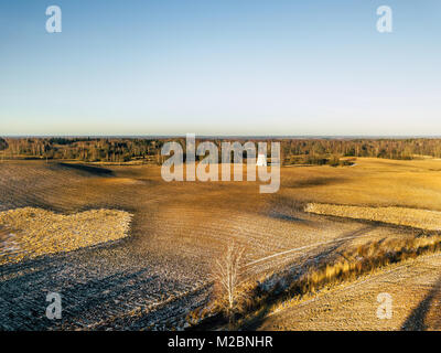 Antenne Drone Fotografie von einem sonnigen Wintertag mit einer schönen Winter Farben der Felder und Windmühle im Hintergrund Stockfoto